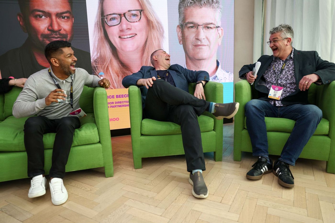 Azlan Raj laughing in a green armchair alongside two other panellists, the speakers' portraits on the screen behind them.