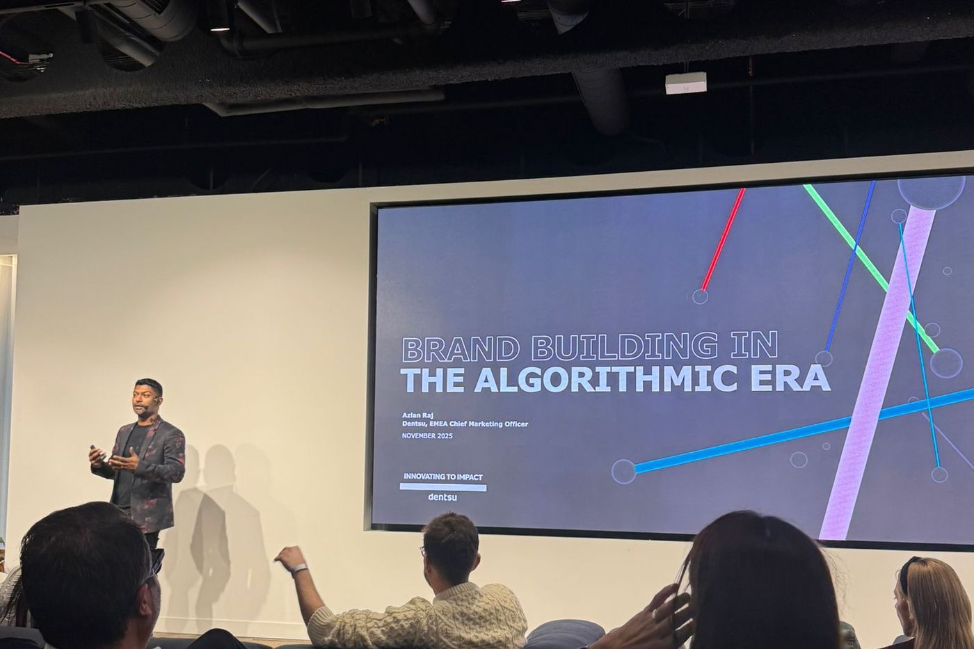 Azlan Raj presenting to a seated audience, beside a screen reading Brand Building in the Algorithmic Era.